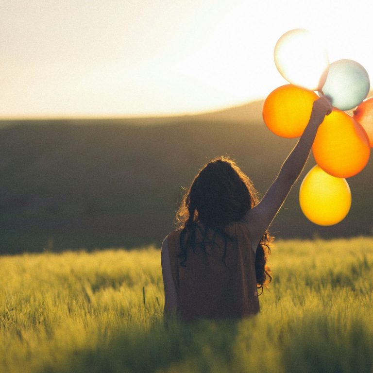 Leicht & unbeschwert - Maria Wadenpohl Psychologische Beratung Online-Coaching Selbstbestimmung für Frauen nach Trennung und Krise Frau mit Luftballons in der Hand läuft durch ein grünes Feld im Abendlicht- Sinnbild für Leichtigkeit